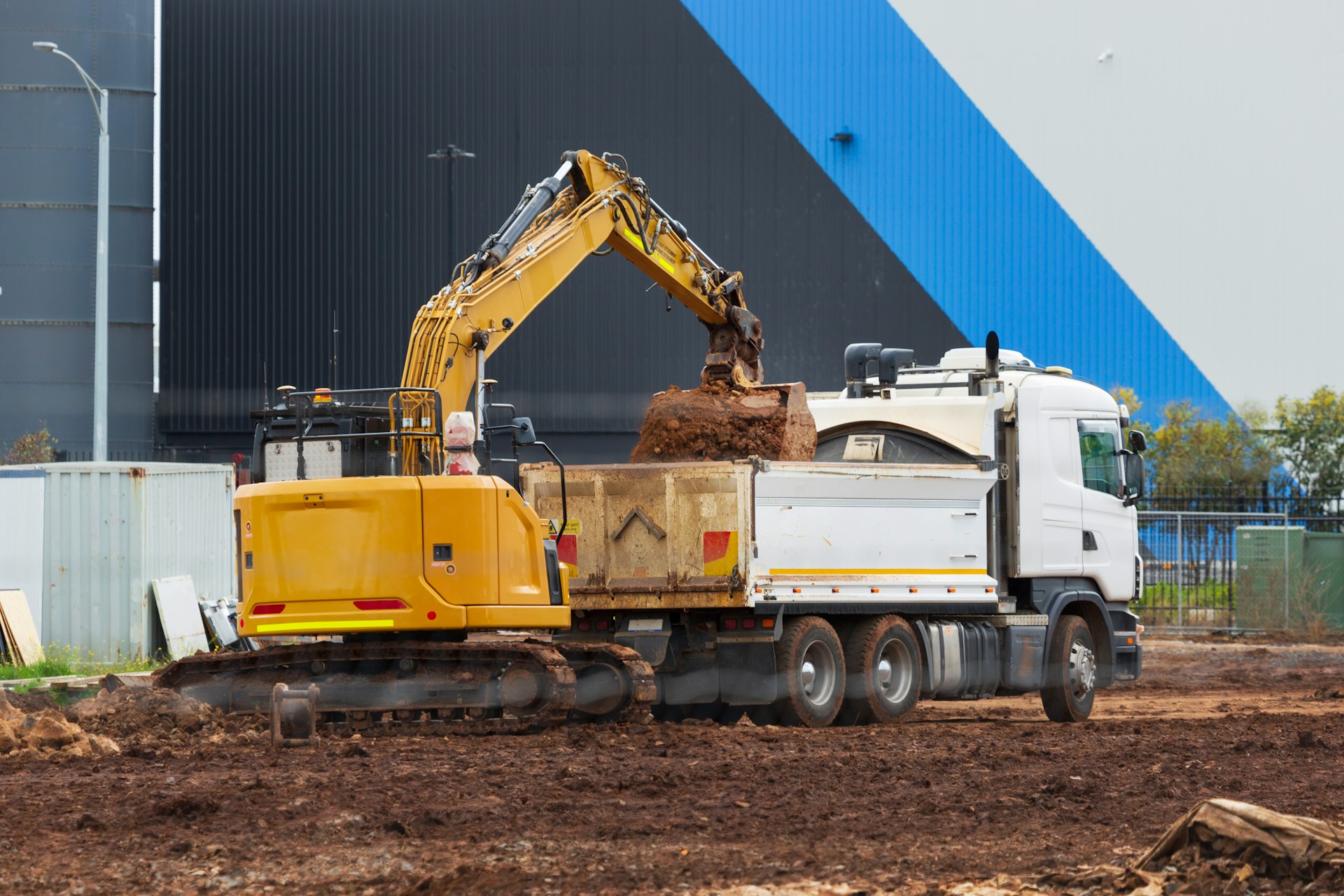 A yellow excavator pours dirt into the back of a white dump truck.