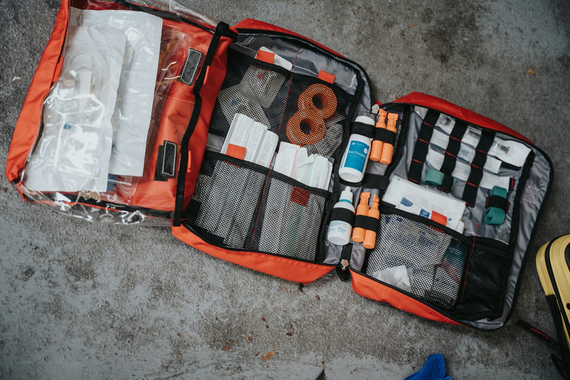 An orange first aid kit, fully stocked with supplies, sits open on a concrete floor.