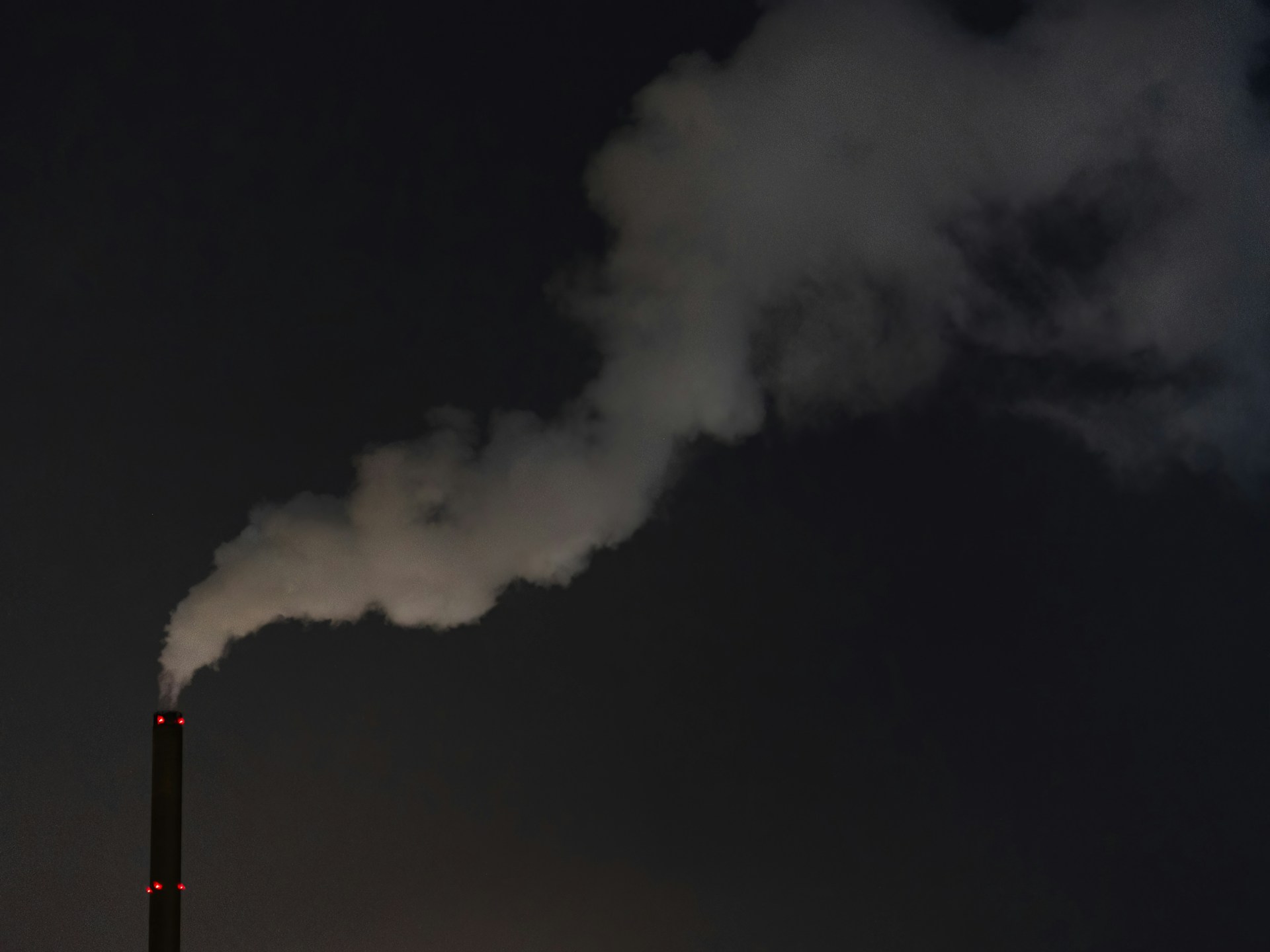 A dark smokestack is releasing white smoke into the night sky.