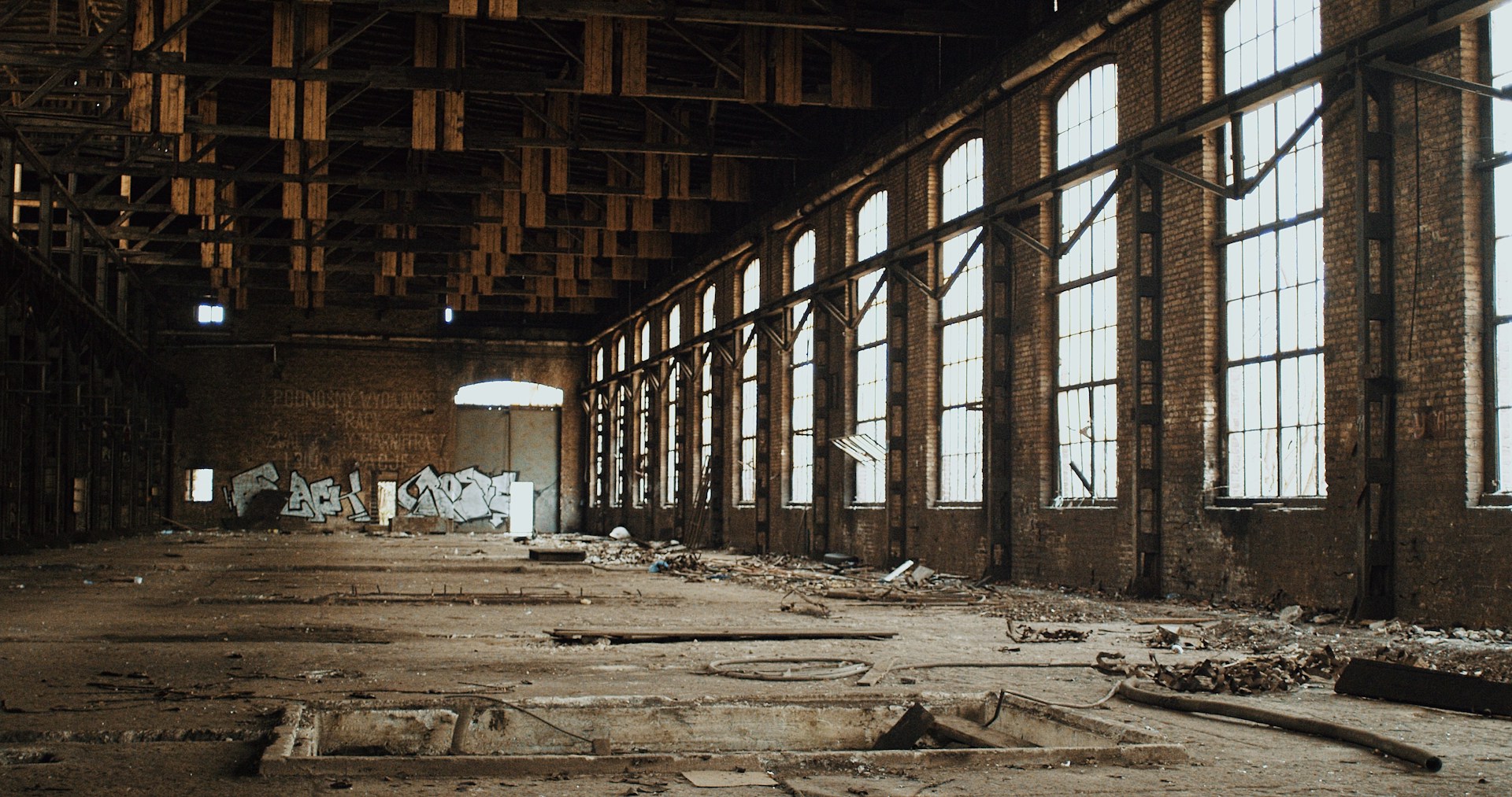Interior of an abandoned warehouse with tall windows lining the wall on the right.