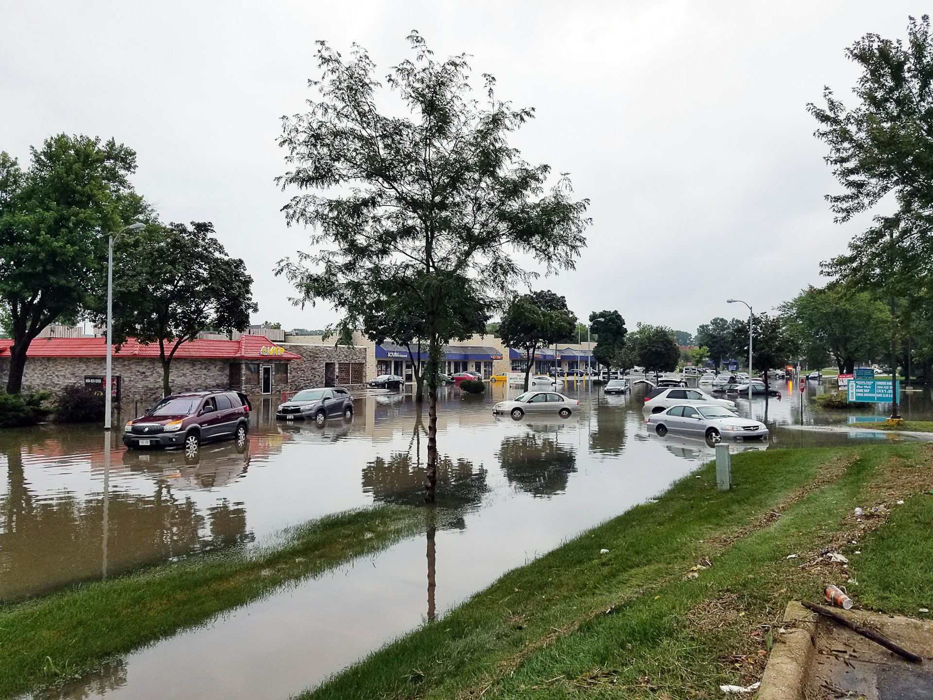 A flooded street lined with cars and shops.