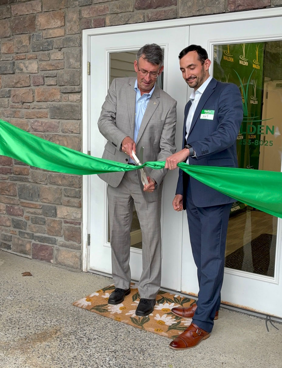 two men cutting a green ribbon in front of the doors of a building