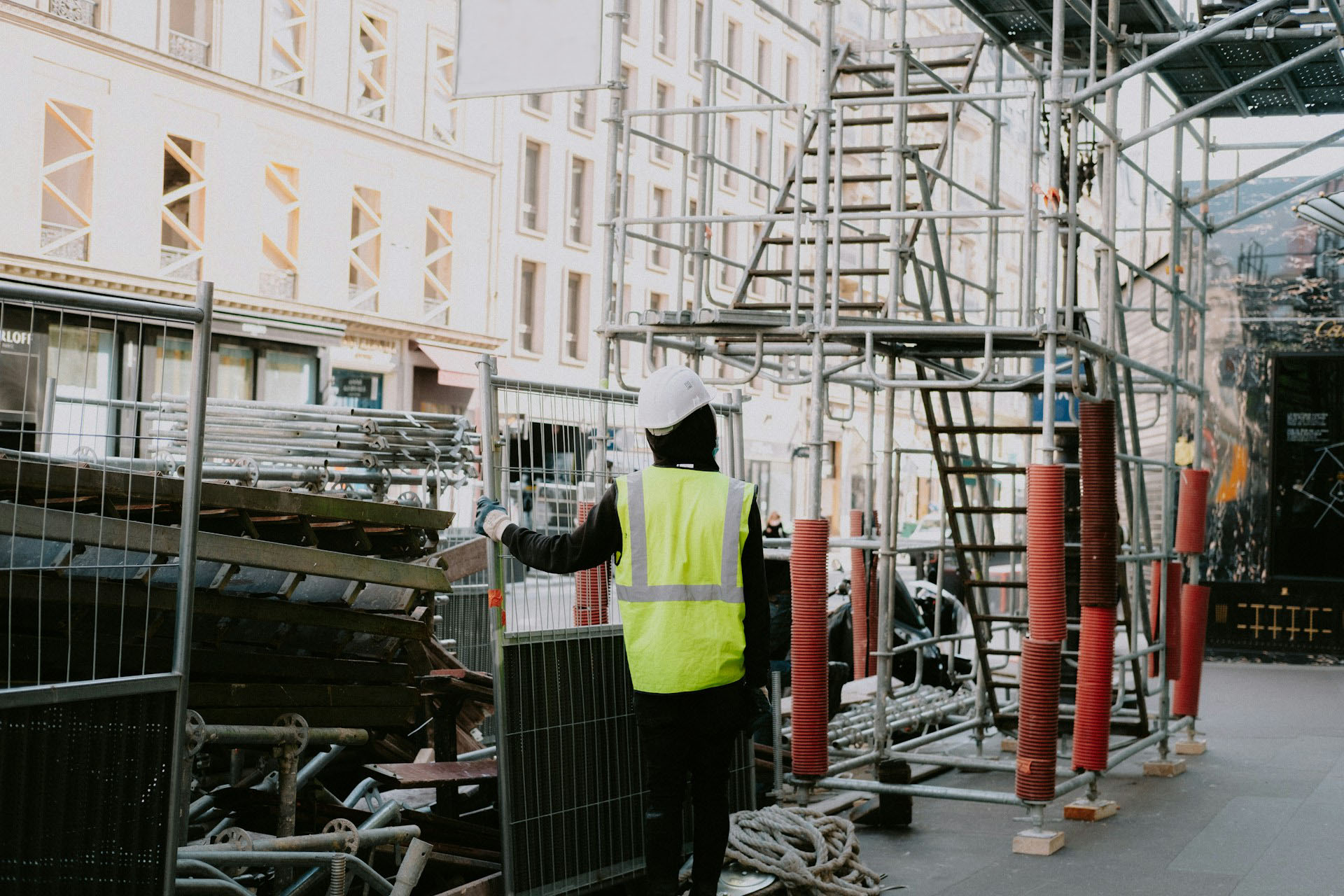 A worker in a neon yellow vest looks up at scaffolding above.
