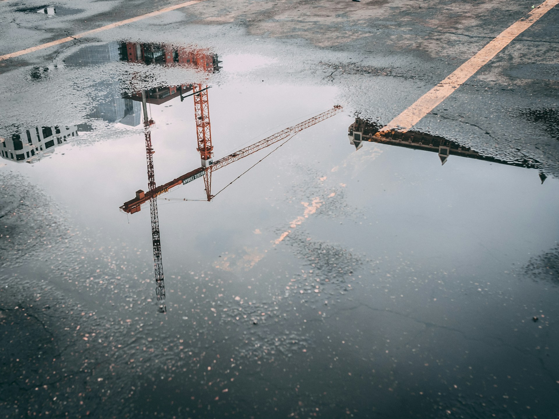An orange construction crane reflected in a puddle.